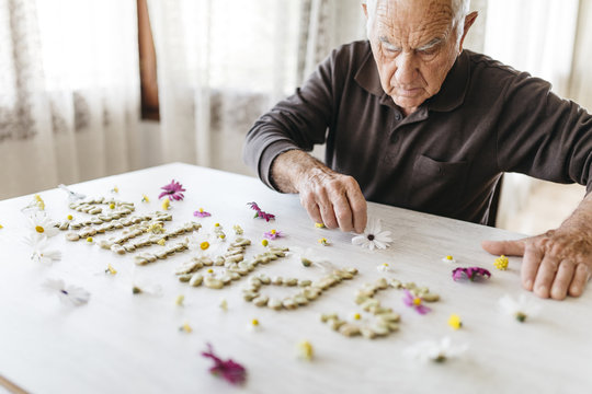 Senior man shaping the word 'spring' with dried beans surrounded by flowers on a table