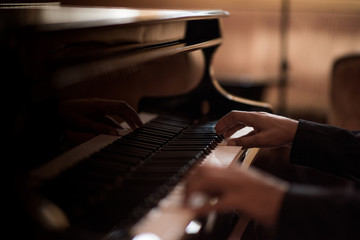 Hands of young man playing piano keys in bar at night
