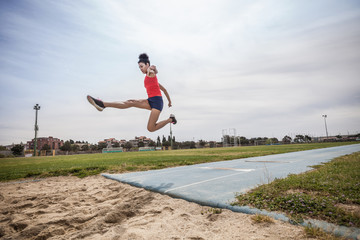 Young female long jumper jumping mid air at sport facility