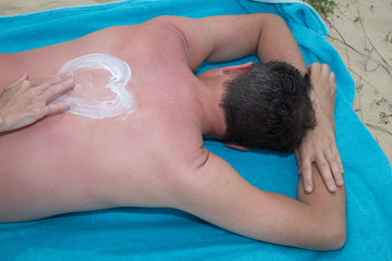 Obraz na płótnie Canvas Applying suncream on the beach with the symbol of love