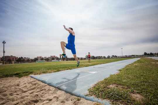 Young Male Long Jumper Jumping Mid Air At Sport Facility