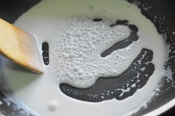 Fototapeta premium coconut milk boiled on non stick pan with bubble and vapour - select focus 