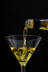 Bottle pouring liqueur into a glass on black background
