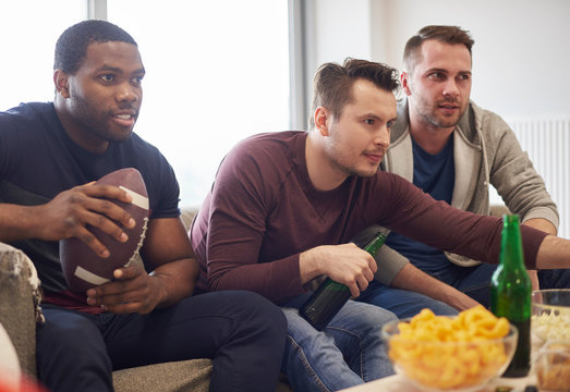 Group of men holding ball watching sports event on television with snacks and beers