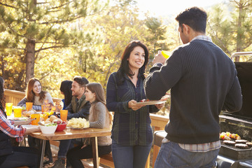 Friends at a table and two talking by grill at a barbecue