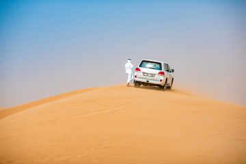 Middle eastern man wearing traditional clothes with off road vehicle parked on desert dune, Dubai, United Arab Emirates