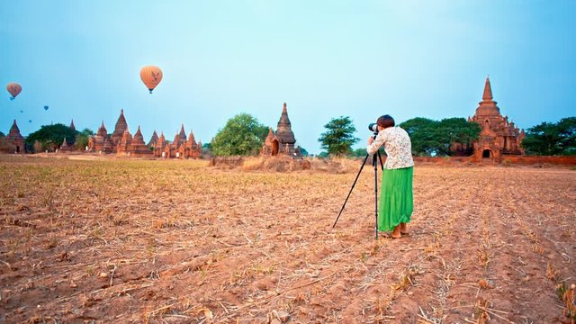 Young woman takes pictures of balloons flying over temples at sunrise in the ancient Bagan city in Myanmar (formerly Burma)