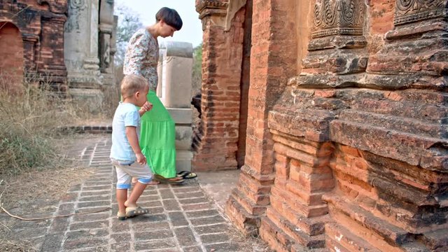 young woman with toddler son removing shoes before entering temple in the ancient Bagan city in Myanmar (formerly Burma)