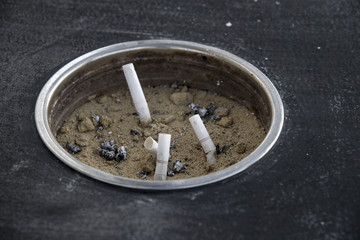 smoked cigarettes in a dirty sand ashtray filled with garbage li