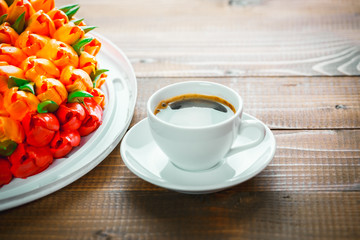 Beautiful background with a Cup of hot coffee with foam and a birthday cake with flowers on wooden background
