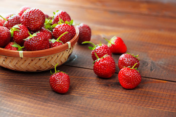 Very beautiful background with fresh strawberries in a wicker round osier basket on old brown wooden background