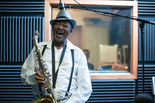Male musician in recording studio, holding saxophone, laughing