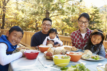 Family at a table on a deck in a forest look to camera