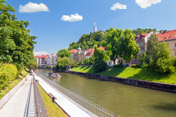 Fototapeta premium Boat on Ljubljanica river and castle raising above on the hilltop, Ljubljana, Slovenia
