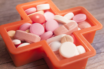 Various medicinal pills  in a cross shape on a wooden background