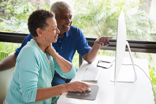 Senior couple sitting at table, using computer