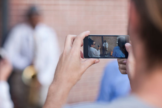 Pedestrian taking photograph of street musician, using smart phone