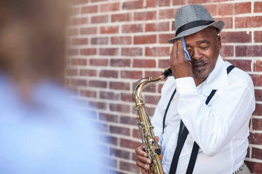 Street musician holding saxophone, wiping brow