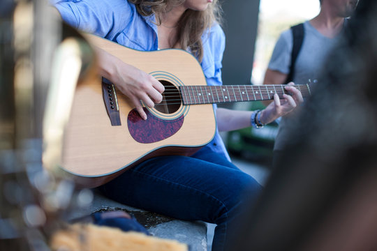 Female street musician playing guitar, mid section