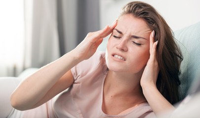 Naklejka premium Young woman with headache lying on couch at home. Casual style indoor shoot