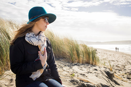 Woman wearing felt hat and sunglasses looking out from dunes, Dillon Beach, California, USA