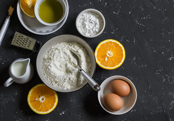 Ingredients for making orange cake with olive oil - flour, eggs, olive oil, powdered sugar on a dark stone background