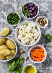 Variety of fresh vegetables in bowls - potatoes, red and cauliflower, spinach, green onions, carrots, nuts, olive oil, cilantro. Raw ingredients. Vegan table. Top view