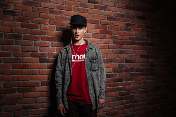 Teenager singing with earphones against red brick wall