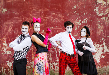 Four mimes standing firmly against the backdrop of a red wall.
