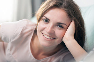Happy young woman lying on couch at home and smiling. Casual style indoor shoot