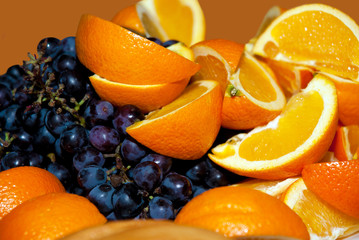  Slices of oranges and grapes closeup. Juicy fresh fruit on a platter. Useful vitamin food for diet. The gifts of nature for people. Tropical and southern fruit blend.