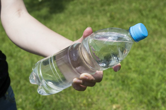 Plastic bottle with water in the men's hands on a background of green grass
