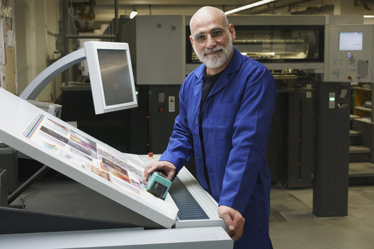 Portrait of smiling mature worker standing by equipment at printing press