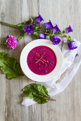Beetroot, beet leaves soup. White plate, wooden background, flowers.