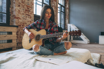 Young woman playing guitar while sitting on bed at home