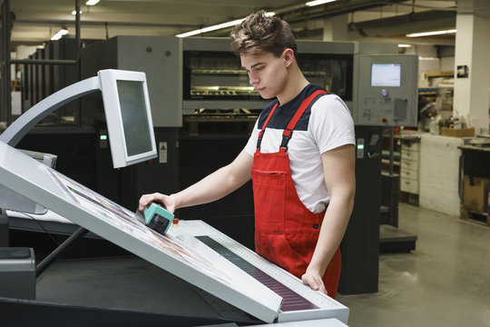Worker checking quality of print with scanner at printing press