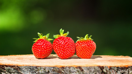 Three ripe, organic strawberry on wooden board