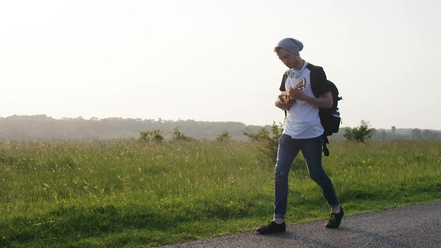 4K Male walking a country road playing his small guitar, in slow motion