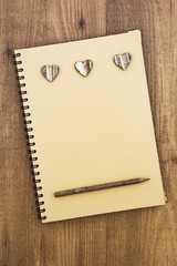 Spiral notebook open with wooden hearts and pencil, on wooden table. Rustic style.