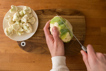 Woman cut cauliflower on cutting board on kitchen table