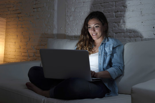 Attractive Relaxed Woman At Home Sitting Happy On Couch Using Laptop At Night