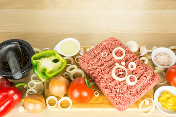 Minced meat on cutting board, pounder and vegetables on wooden b