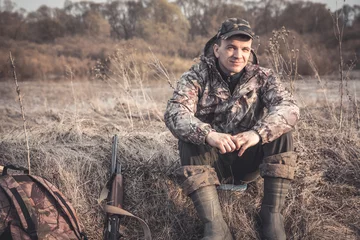Crédence de cuisine en verre imprimé Chasser Hunter man in rural field with shotgun and backpack during hunting season  