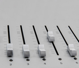 closeup side view of chrome slide buttons on metallic surface of a music mixer