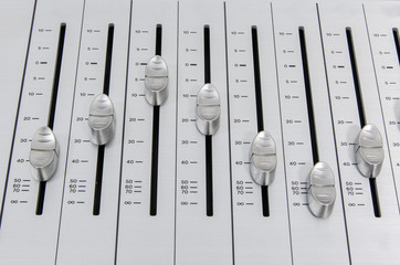 closeup view of chrome slider buttons forming a wave pattern on metallic surface of a sound mixer