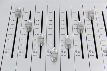 closeup view  of chrome slider buttons forming a 'V' sign on metallic surface of a sound mixer