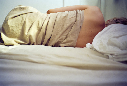 Woman in bed wrapped in crumpled sheet