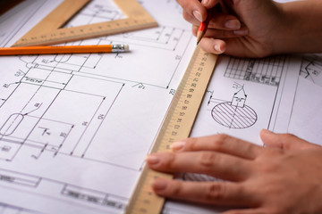 Girl architect draws a plan, graph, design, geometric shapes by pencil on large sheet of paper at office desk. Soft focus