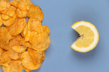 Potato chips versus juicy yellow lemon. Poor nutrition and healthy food on the blue background. Yellow fresh fruit in front of fatty fried chips.