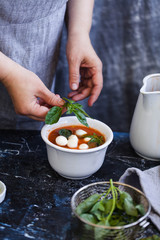 Gazpacho bowl with caprese salad making for female hand. Mediterranean food.